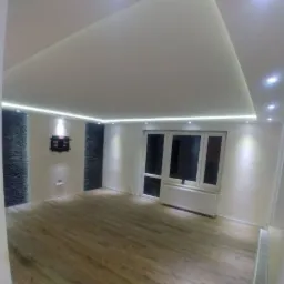 Nowoczesne wnętrze pokoju z drewnianą podłogą, białymi ścianami, dekoracyjną ścianą z kamienia i podwieszanym sufitem z oświetleniem LED.