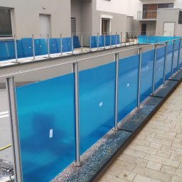 ROB TECH Robert Przewodowski - Długa, zewnętrzna balustrada ze stali nierdzewnej z niebieskimi panelami ochronnymi, zamontowana wzdłuż chodnika przy nowoczesnym budynku mieszkalnym.