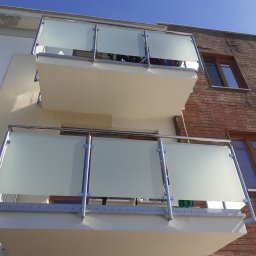 ROB TECH Robert Przewodowski - Dwa balkony z balustradami ze stali nierdzewnej i mlecznego szkła na tle budynku z drewnianą elewacją. Widok z dołu, słoneczny dzień.