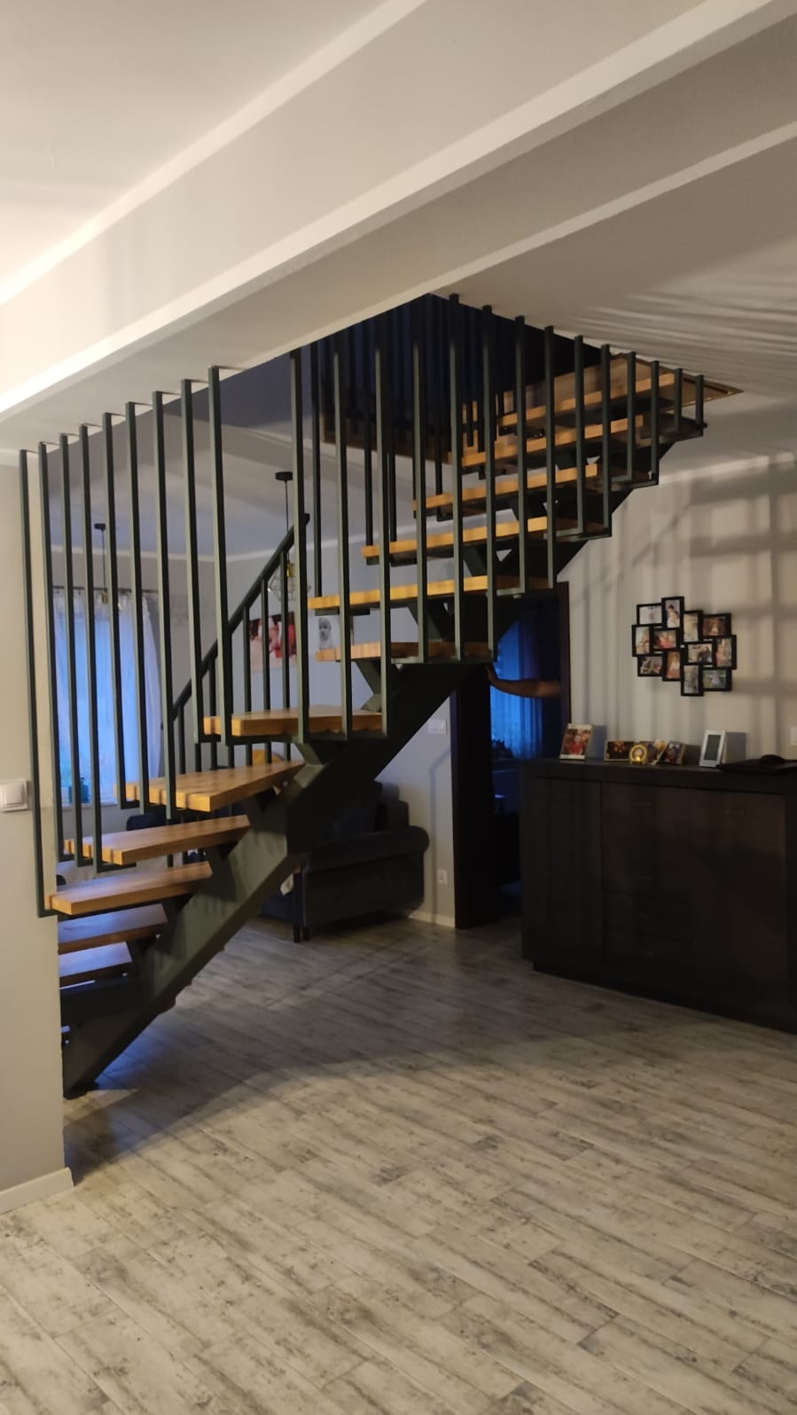 Nowoczesne schody metalowe z drewnianymi stopniami, czarne pionowe balustrady, minimalistyczny design, widok z dołu, wnętrze domu, jasne ściany, podłoga drewnopodobna.