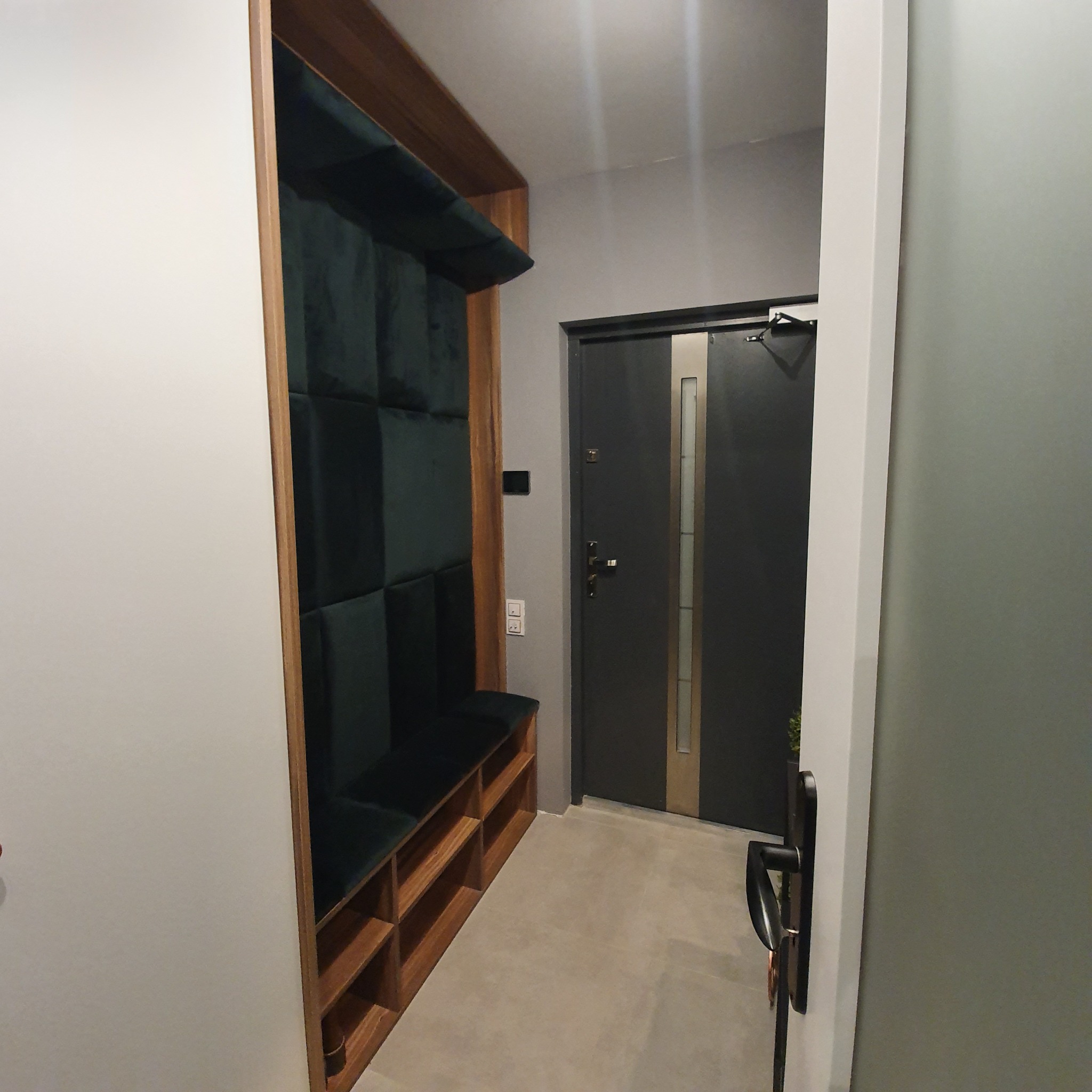 Wnęka z tapicerowanym siedziskiem i półkami w przedpokoju, obok drzwi wejściowych.