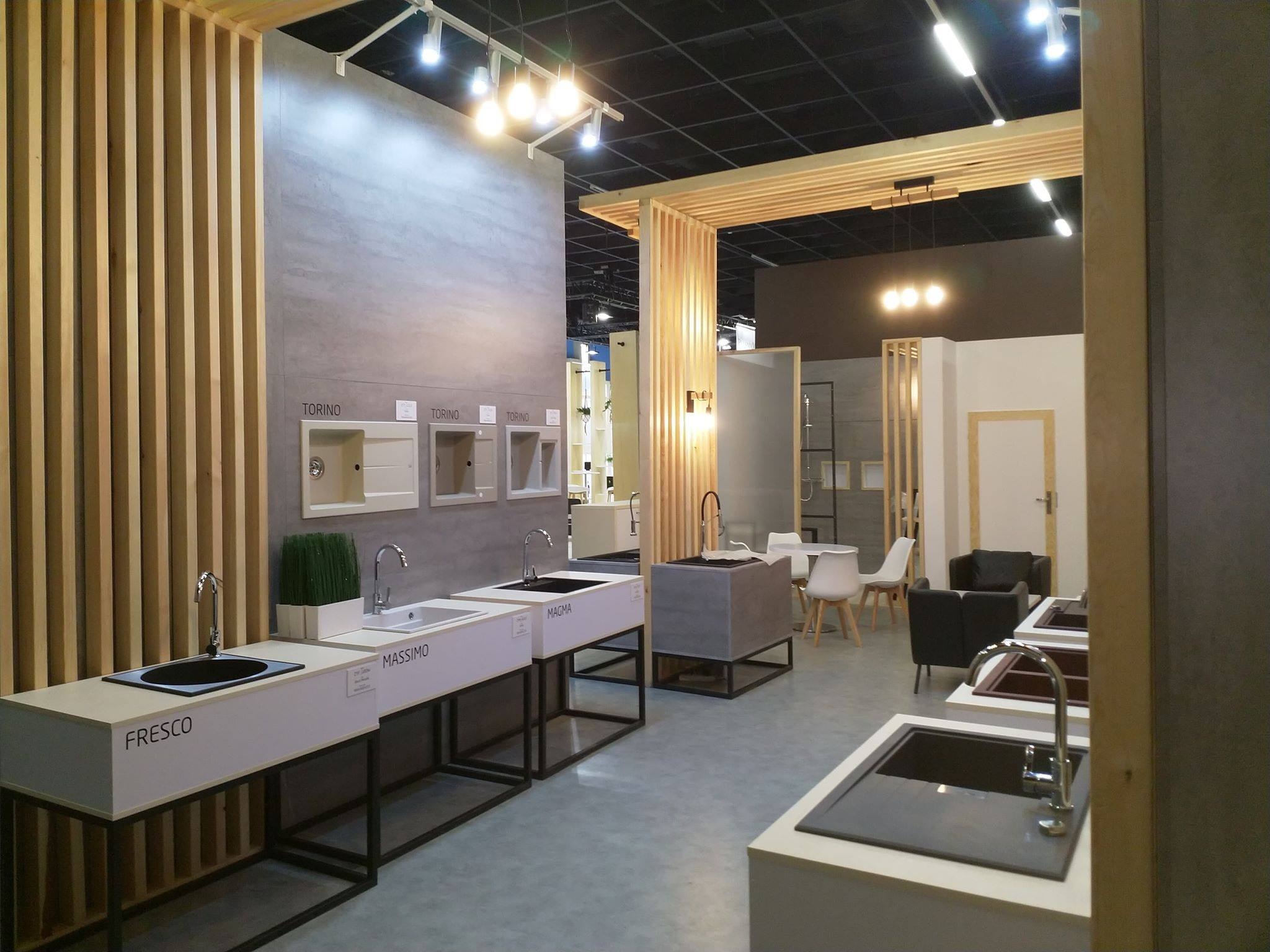 Ekspozycja umywalek i baterii różnych producentów (Fresco, Massimo, Magma, Torino) na stoisku targowym z drewnianymi elementami dekoracyjnymi i oświetleniem punktowym.