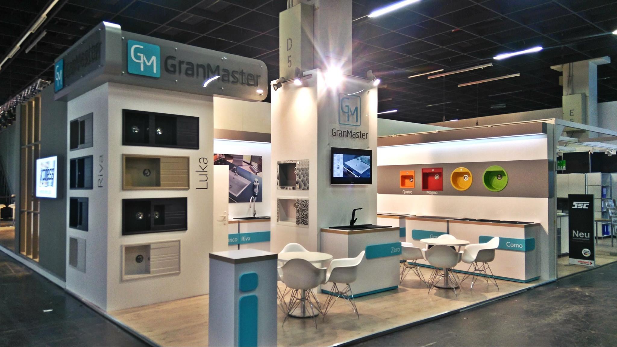 Ekspozycja producenta zlewów i armatury na targach, prezentująca różne modele zlewów w zabudowie, w tym zlewy z ociekaczem w kolorach czarnym, beżowym i szarym, oraz okrągłe zlewy w kolorach...