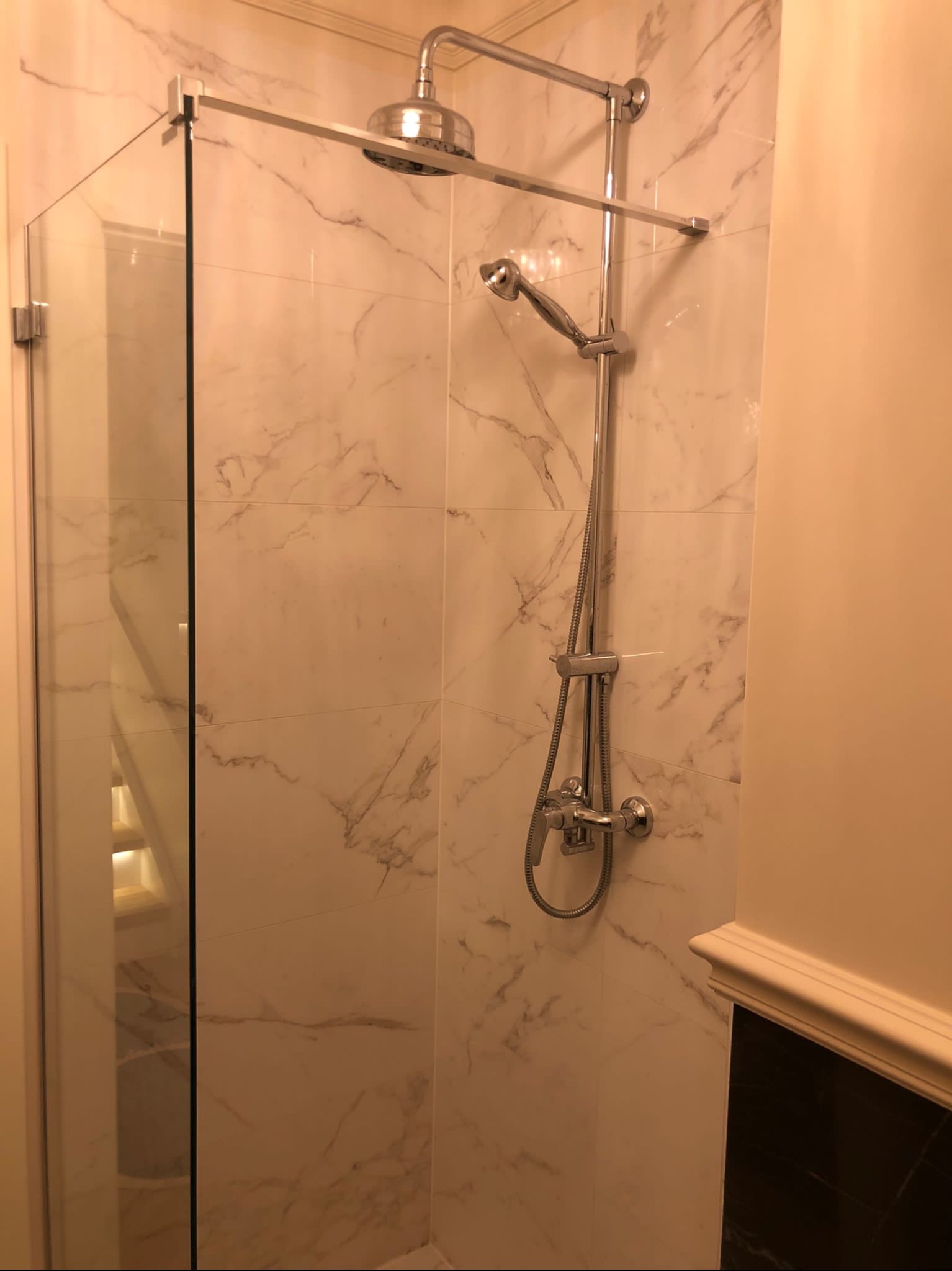 Wykończona kabina prysznicowa ze szklaną ścianką i marmurowymi płytkami w Świnoujściu, widoczny zestaw natryskowy z deszczownicą.