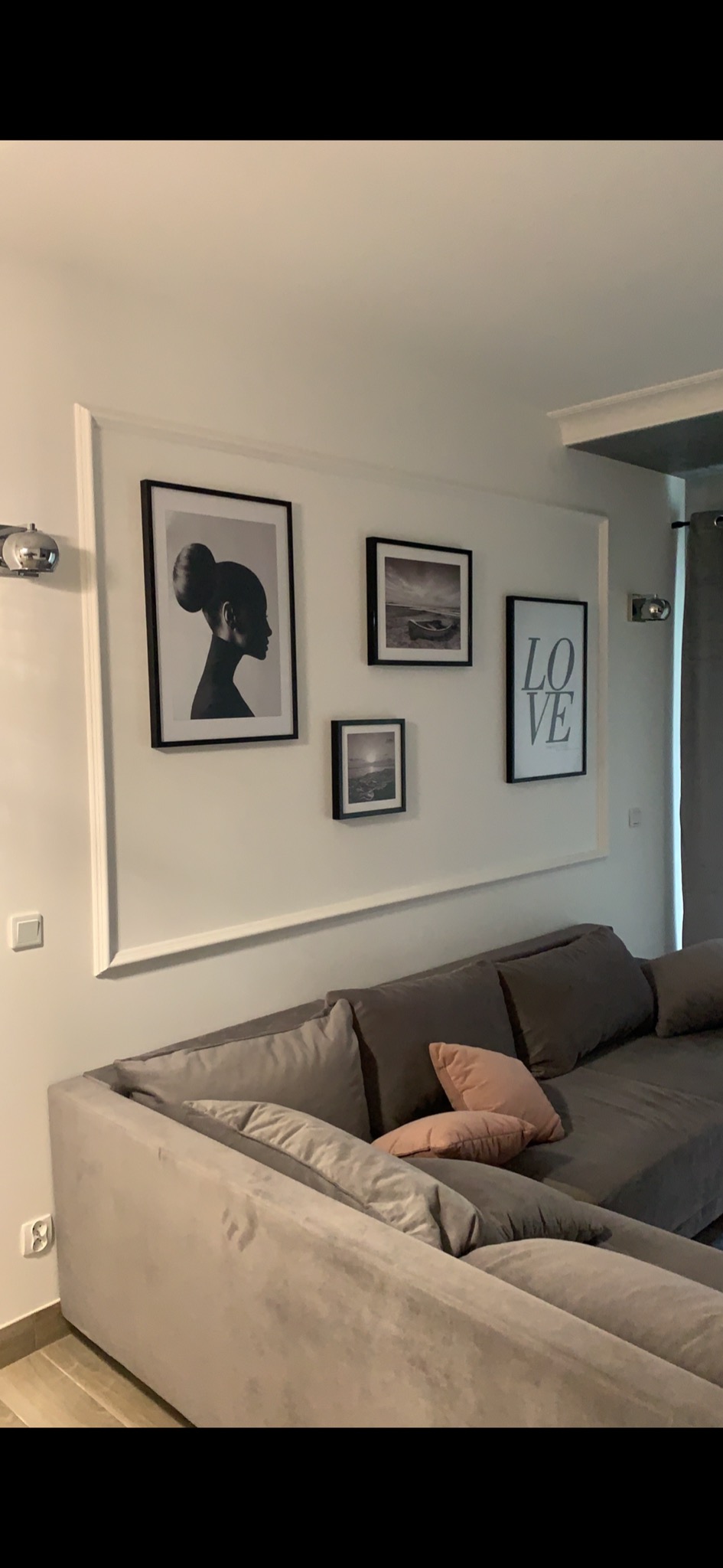Szary narożnik z poduszkami w salonie z galerią czarno-białych obrazów w białej ramie na ścianie.