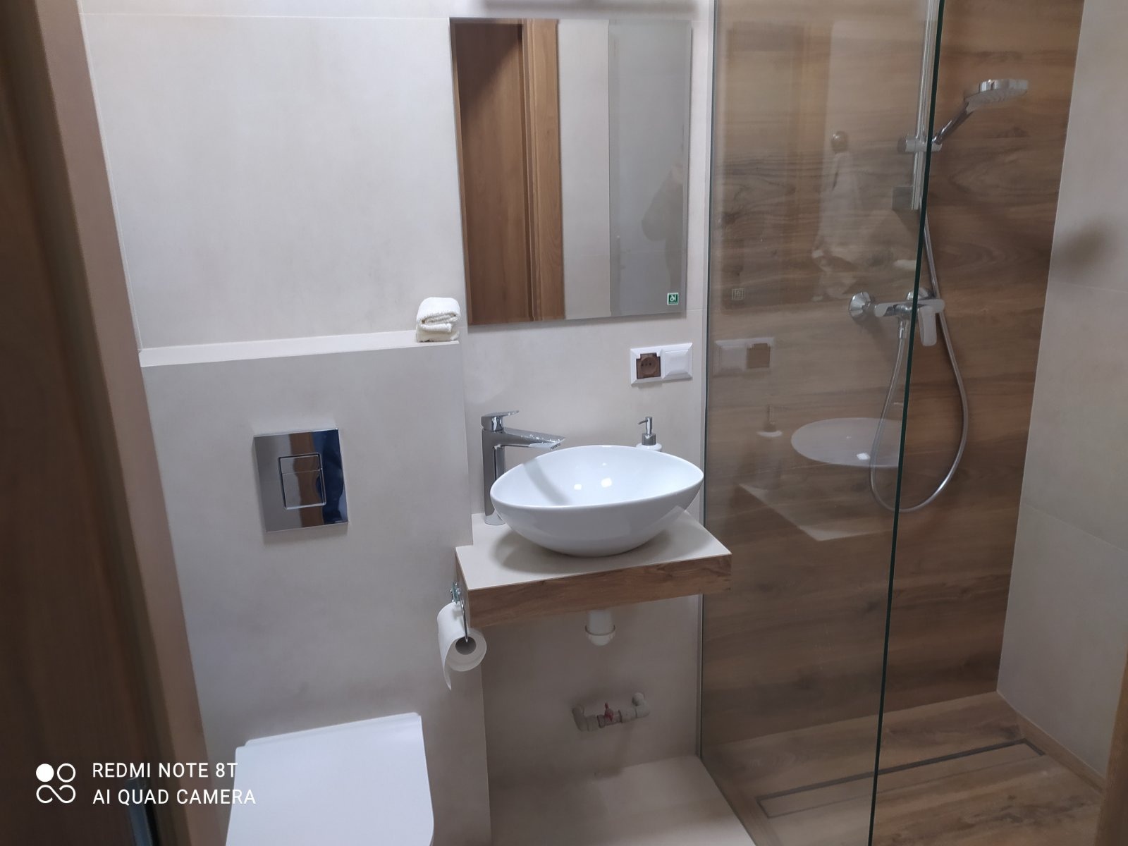 Nowoczesna łazienka z kabiną prysznicową typu walk-in, umywalką nablatową na drewnianym blacie i chromowaną armaturą, minimalistyczny design.