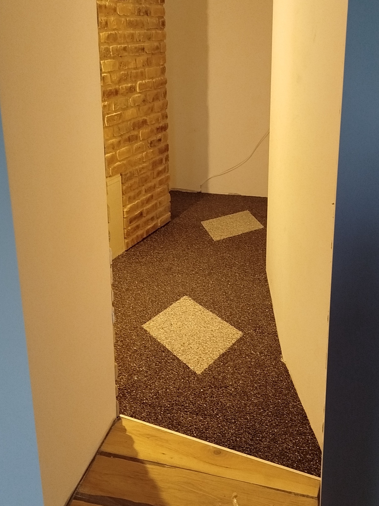 Wykończone wnętrze z dekoracyjną ścianą z cegły i podłogą z wzorem kwadratów. Widok zza framugi drzwi.