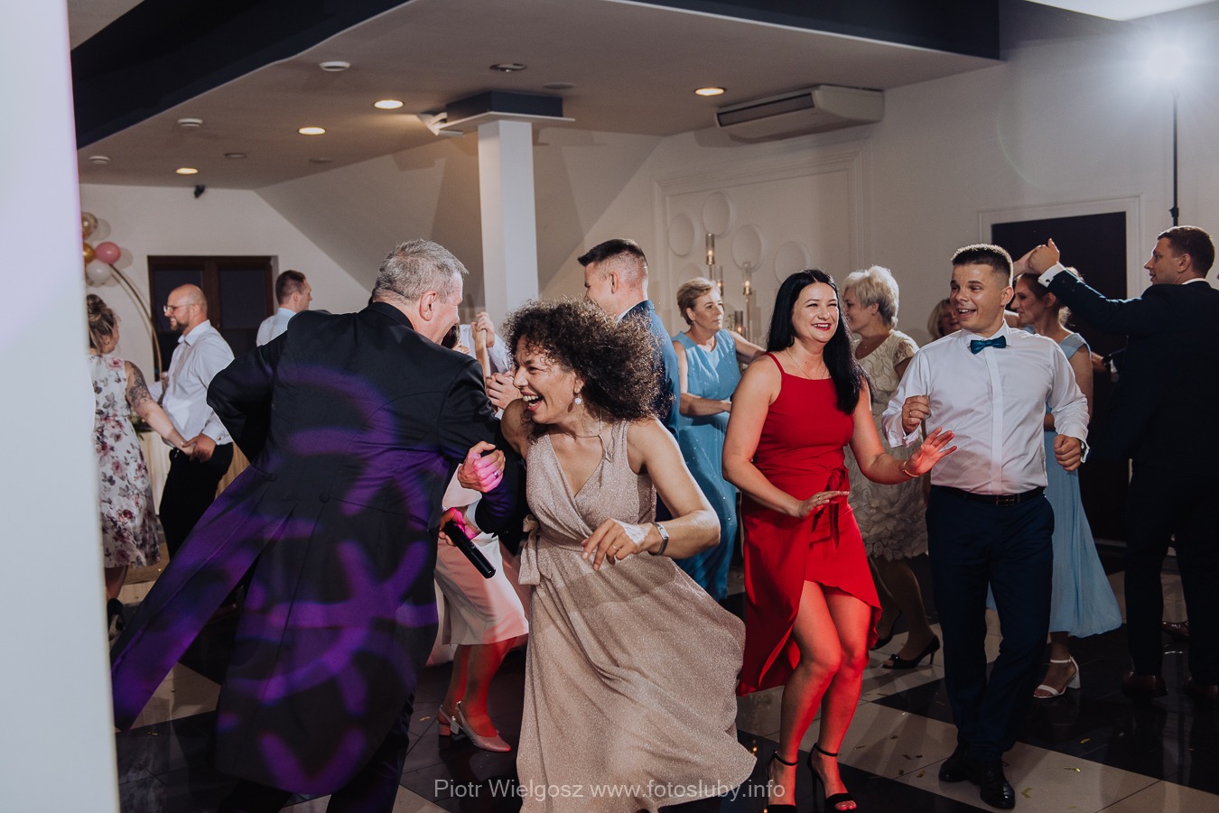 Rozbawieni goście weselni tańczą na parkiecie podczas przyjęcia, oświetleni kolorowymi światłami.