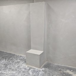 Regionalna grupa budowlana Mariusz pokutowski - Szara, gładka ściana z wystającym filarem w rogu pomieszczenia. Minimalistyczne wykończenie wnętrza, surowy styl. Podłoga w odcieniach szarości.