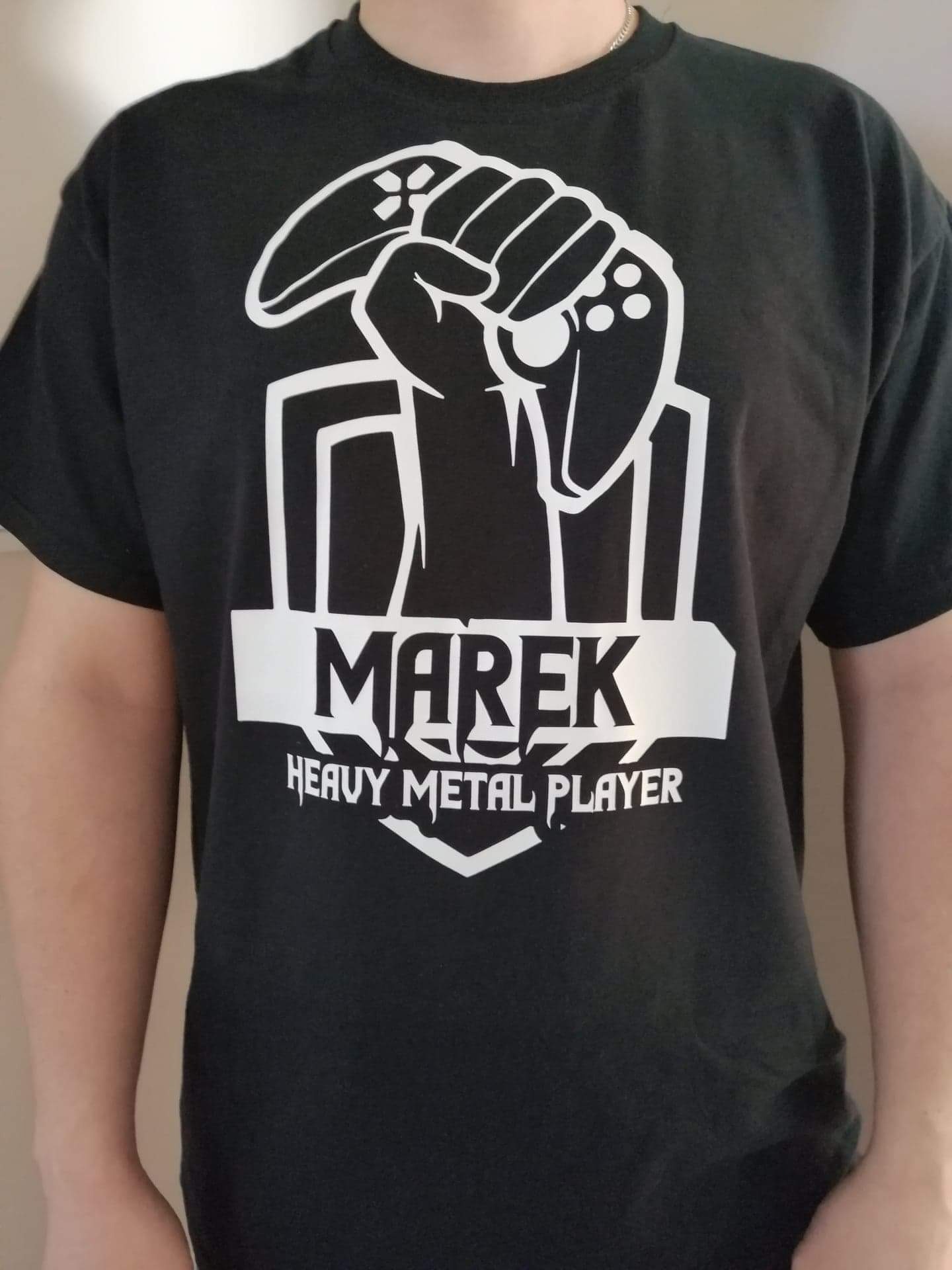 Czarna koszulka z białym nadrukiem: dłoń trzymająca kontroler do gier, imię 'Marek' i napis 'Heavy Metal Player'.