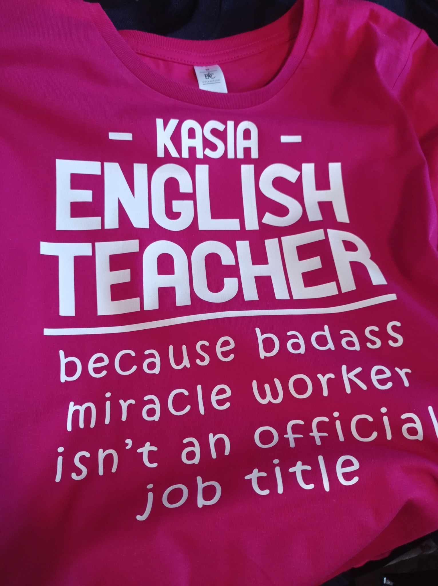 Różowa koszulka z białym nadrukiem 'KASIA - ENGLISH TEACHER because badass miracle worker isn't an official job title'.