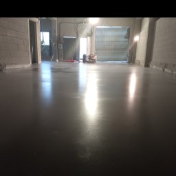 Profest Posadzki Przemysłowe - Świeżo wylana, gładka posadzka przemysłowa w surowym wnętrzu hali z widocznymi maszynami i narzędziami w tle.