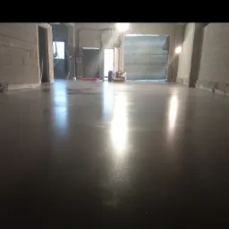 Świeżo wylana, gładka posadzka przemysłowa w surowym wnętrzu hali z widocznymi maszynami i narzędziami w tle.