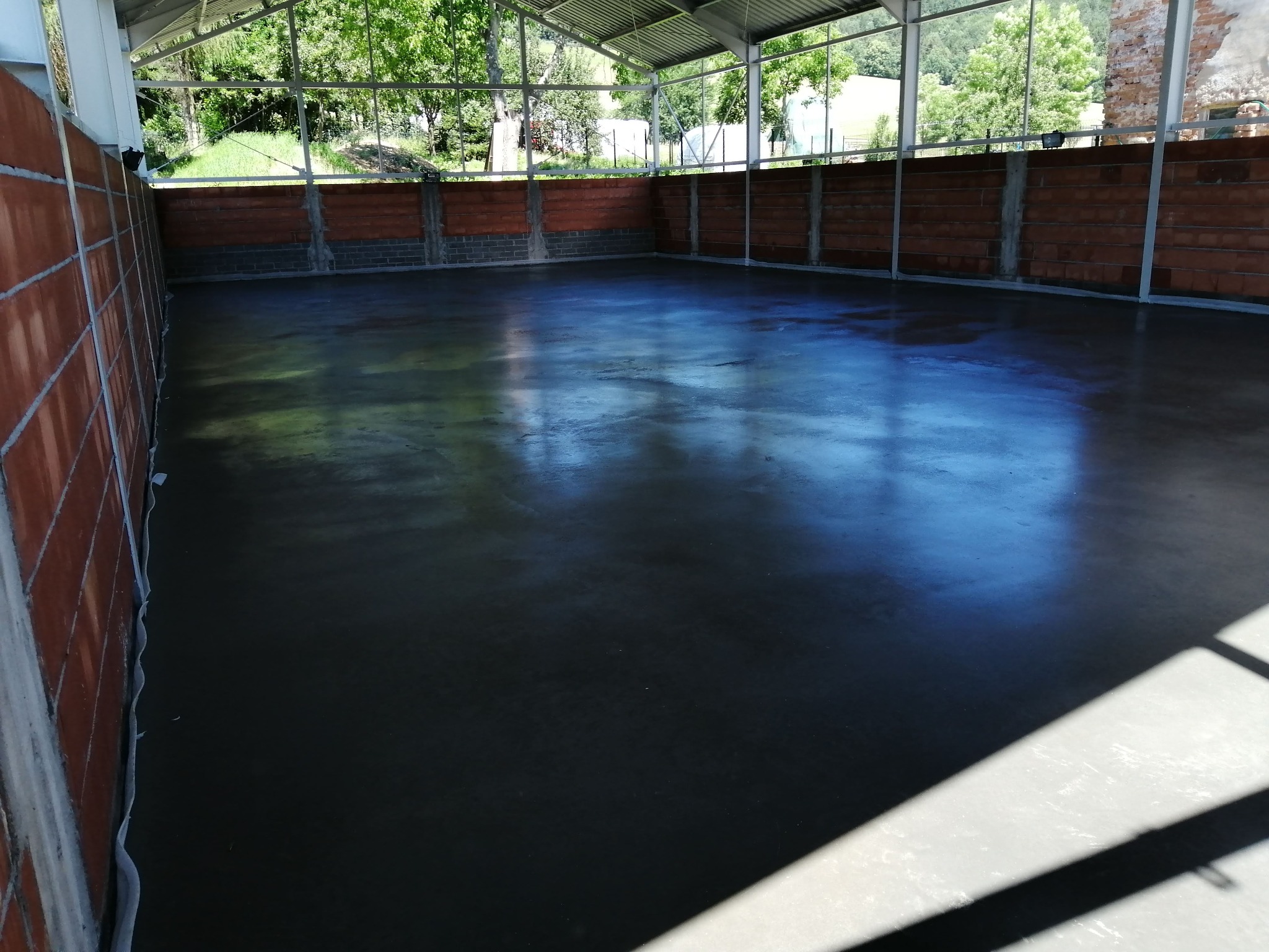 Świeżo wylana, gładka, ciemnoszara posadzka w hali z ceglanymi ścianami, widoczne refleksy światła na powierzchni.