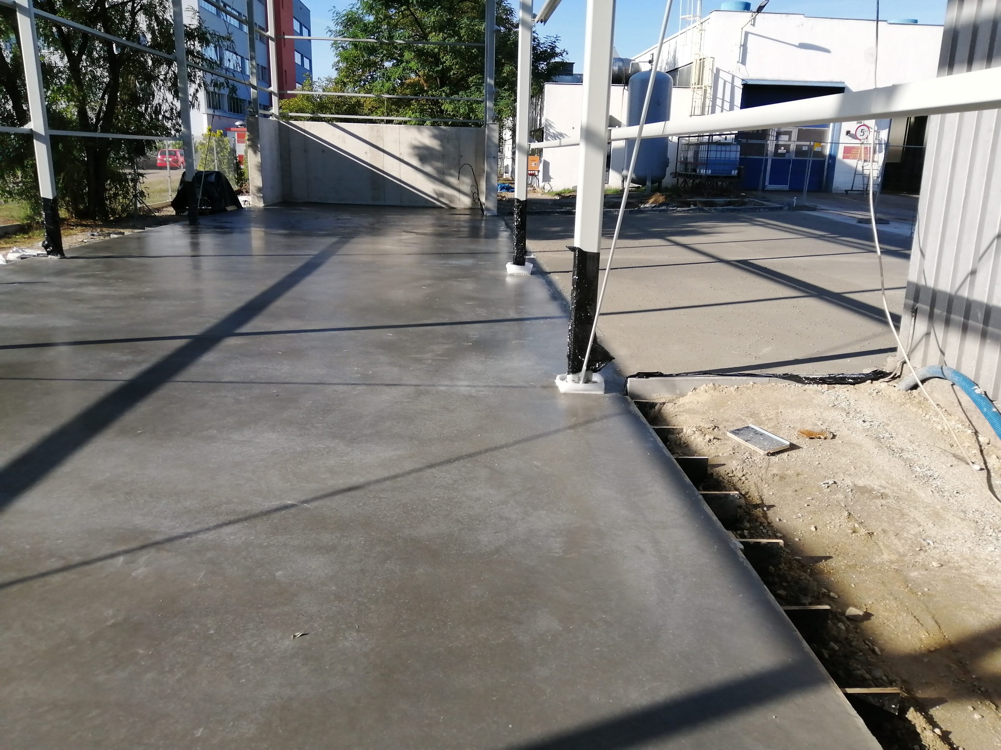 Świeżo wylana, gładka posadzka przemysłowa w Strużynie, częściowo osłonięta metalową konstrukcją, z widocznym fragmentem przygotowanego podłoża do dalszych prac.