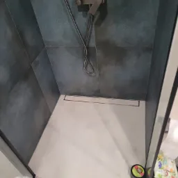 Nowoczesny prysznic z ciemnymi, wzorzystymi płytkami, odpływem liniowym i deszczownicą w kolorze grafitowym, widok z góry.