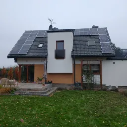 Nowoczesny dom jednorodzinny z panelami słonecznymi na dachu, widok z ogrodu w jesiennej scenerii.