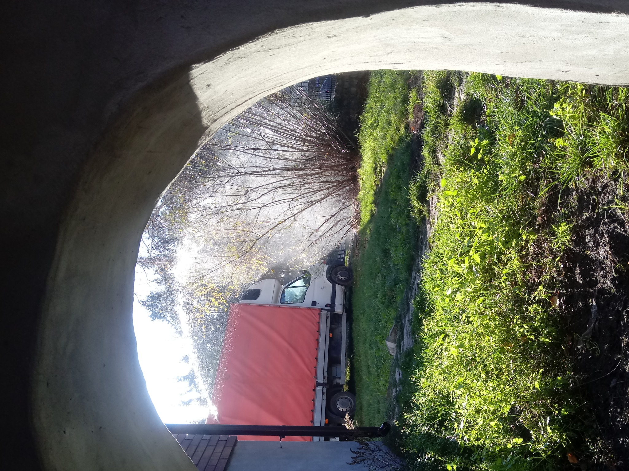 Wiercenie studni widziane z wnętrza betonowej rury, w tle ciężarówka z czerwoną plandeką i woda tryskająca podczas wiercenia.