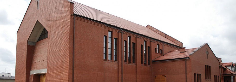 Zewnętrzny widok nowo wybudowanego, dwukondygnacyjnego budynku z czerwonej cegły z ukośnym oknem i dachem z czerwonej dachówki ceramicznej.
