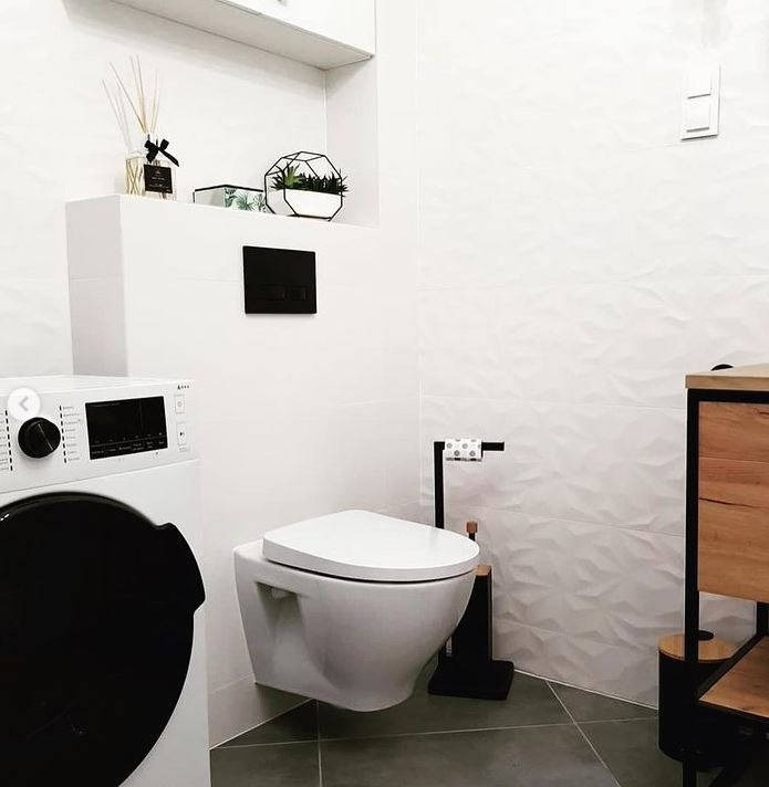 Nowoczesna łazienka w bieli i szarości z wiszącą toaletą, pralką i dekoracyjnymi płytkami ściennymi z efektem 3D.