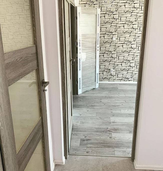 Wrocław: Widok na wnętrze po montażu drzwi wewnętrznych z drewnianymi ościeżnicami i przeszklonymi skrzydłami, jedna z nich jeszcze w folii ochronnej, na podłodze panele imitujące drewno, ściana...