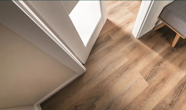 Beżowe panele podłogowe ułożone w jodełkę, widoczne przez otwarte białe drzwi, z fragmentem krzesła w tle, Wrocław.