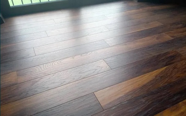 Ułożone ciemne panele podłogowe z widocznymi słojami drewna, oświetlone naturalnym światłem wpadającym przez okno.