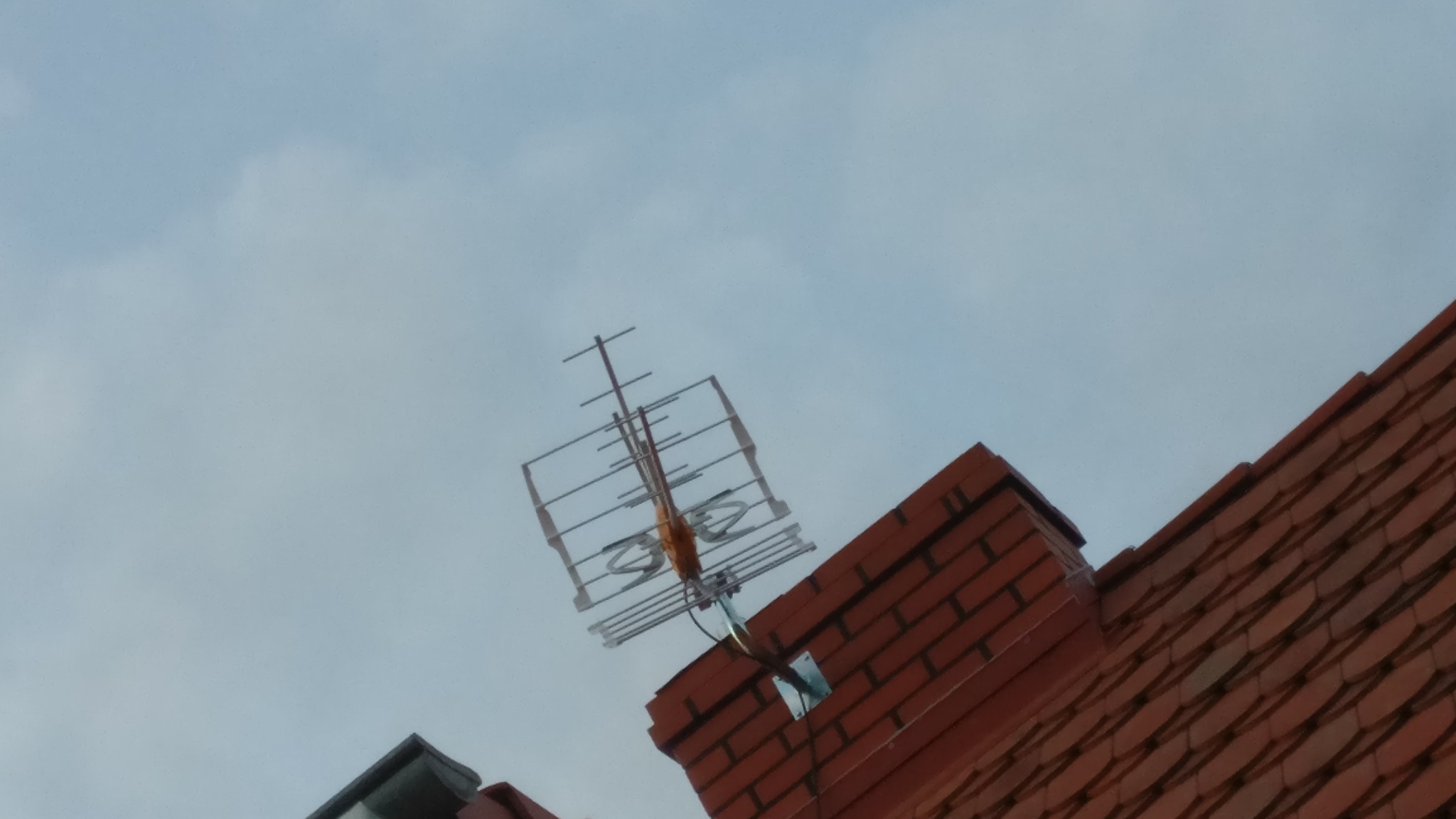 Antena telewizyjna zamontowana na dachu z czerwonej dachówki, widoczna pod pochmurnym niebem.