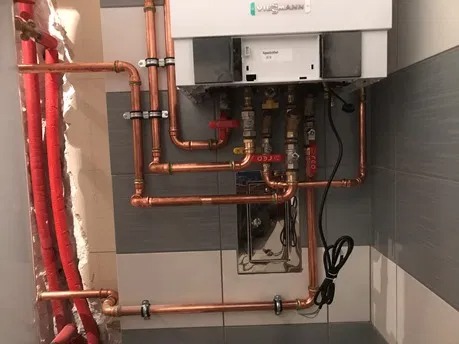 Nowa instalacja grzewcza z piecem Viessmann, miedziane rury i zawory na tle szarych płytek.