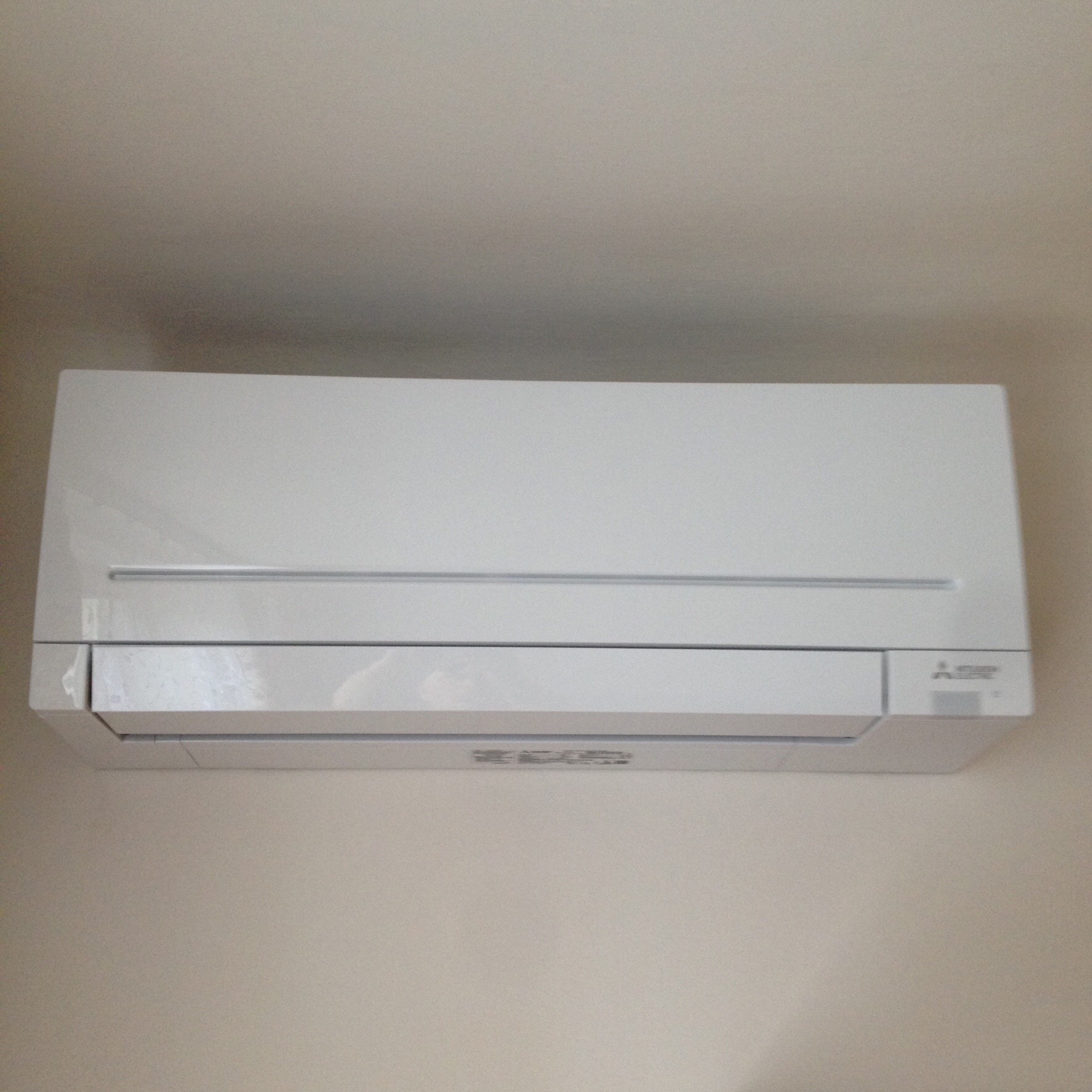 Biała jednostka wewnętrzna klimatyzacji Mitsubishi zamontowana na jasnej ścianie.