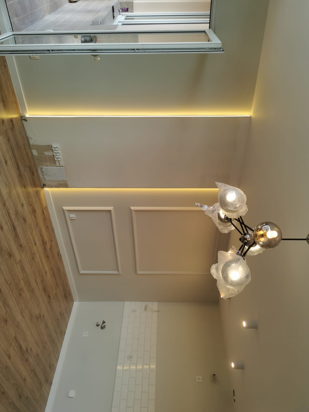 Nowoczesne wnętrze z oświetleniem LED w suficie, dekoracyjnymi panelami ściennymi i lampą w folii ochronnej, widok z dołu.