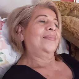 Kobieta z blond włosami leży na kwiecistej poduszce i uśmiecha się, widoczna część ramienia i czarny top.