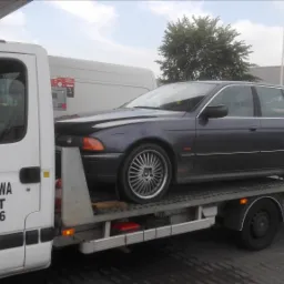 Laweta z ciemnoszarym BMW kombi na platformie, w tle salon Suzuki.