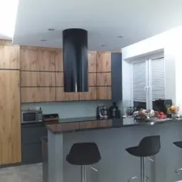 Nowoczesna kuchnia z drewnianymi szafkami, czarnym okapem cylindrycznym i szarym blatem barowym z hokerami.