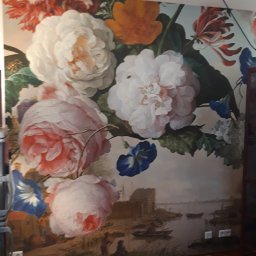 Piotr i Paweł - usługi remontowo wykończeniowe - Ściana z fototapetą przedstawiającą bukiet kwiatów w stylu holenderskim na tle pejzażu z łodziami, uzupełniona drewnianą podłogą i czarnym punktowym oświetleniem sufitowym.