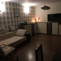 Piotr i Paweł - usługi remontowo wykończeniowe - Pokój dzienny po odświeżeniu: ściana w szaro-białą kratę, jasna sofa z poduszkami, ciemna drewniana podłoga i meble w odcieniach bieli i brązu.