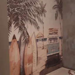 Ściana z fototapetą przedstawiającą plażę z palmami, deskami surfingowymi i busem z deskami na dachu, widoczne niedoskonałości w narożniku i przy podłodze.