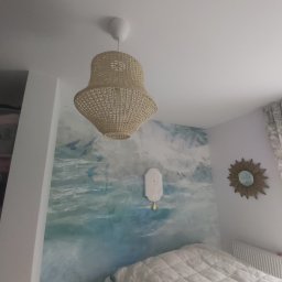 Piotr i Paweł - usługi remontowo wykończeniowe - Sypialnia z tapetą imitującą morski krajobraz, wiklinowa lampa wisząca i lustro w kształcie słońca na ścianie.