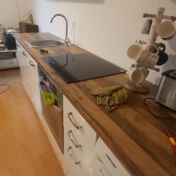 Piotr i Paweł - usługi remontowo wykończeniowe - Wnętrze kuchni z białymi szafkami, drewnianym blatem, czarną płytą indukcyjną, zlewozmywakiem i stojakiem na kubki, z pralką pod blatem