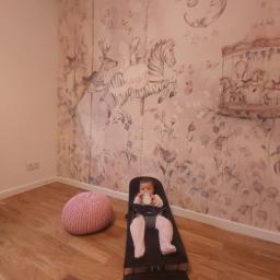 Piotr i Paweł - usługi remontowo wykończeniowe - Pokój dziecięcy w Karczewie z tapetą przedstawiającą motywy karuzeli, w foteliku siedzi dziecko pijące mleko, obok pufa.