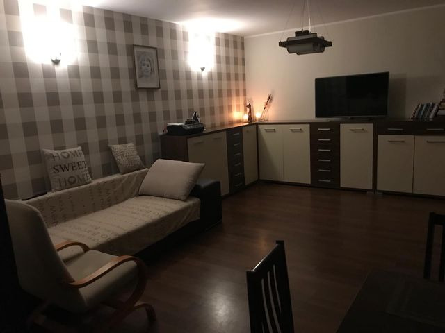 Pokój dzienny po odświeżeniu: ściana w szaro-białą kratę, jasna sofa z poduszkami, ciemna drewniana podłoga i meble w odcieniach bieli i brązu.