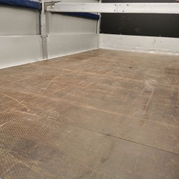 TRANS-TOM Tomasz Małka - Pusta przestrzeń ładunkowa busa z podłogą o wzorze plastra miodu i metalowymi ścianami, widoczne ślady użytkowania.