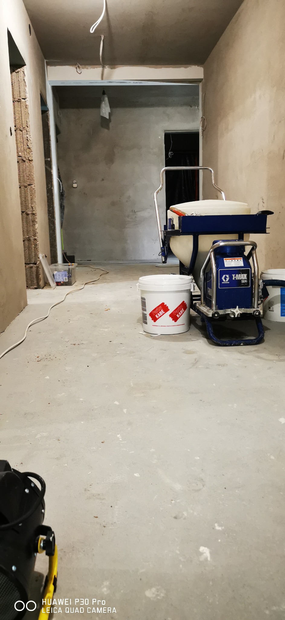 Przygotowania do prac wykończeniowych: agregat malarski Graco T-Max 506, wiadro z farbą Farby Kabe, surowe ściany i sufity w trakcie szpachlowania, widoczne kable elektryczne.