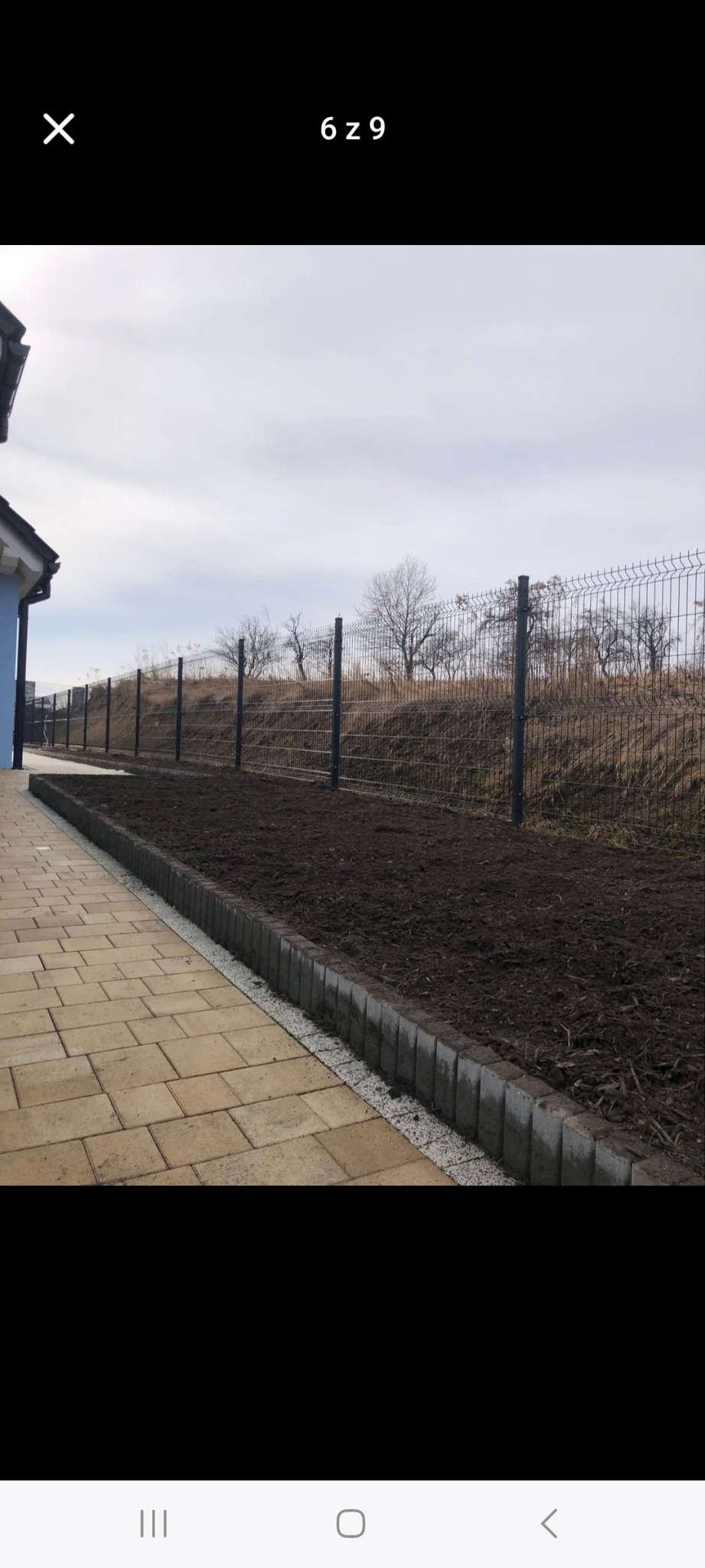 Przygotowany teren pod trawnik z obrzeżami i siatką ogrodzeniową w tle. Świeżo przekopana ziemia, kostka brukowa i szara siatka tworzą estetyczne wykończenie działki.