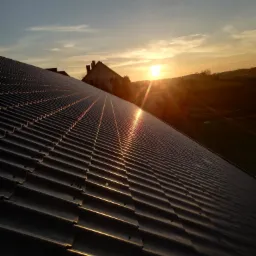 Nowy, metalowy dach modułowy w kolorze grafitowym, widziany pod kątem podczas zachodu słońca, z widocznymi promieniami odbijającymi się od powierzchni.