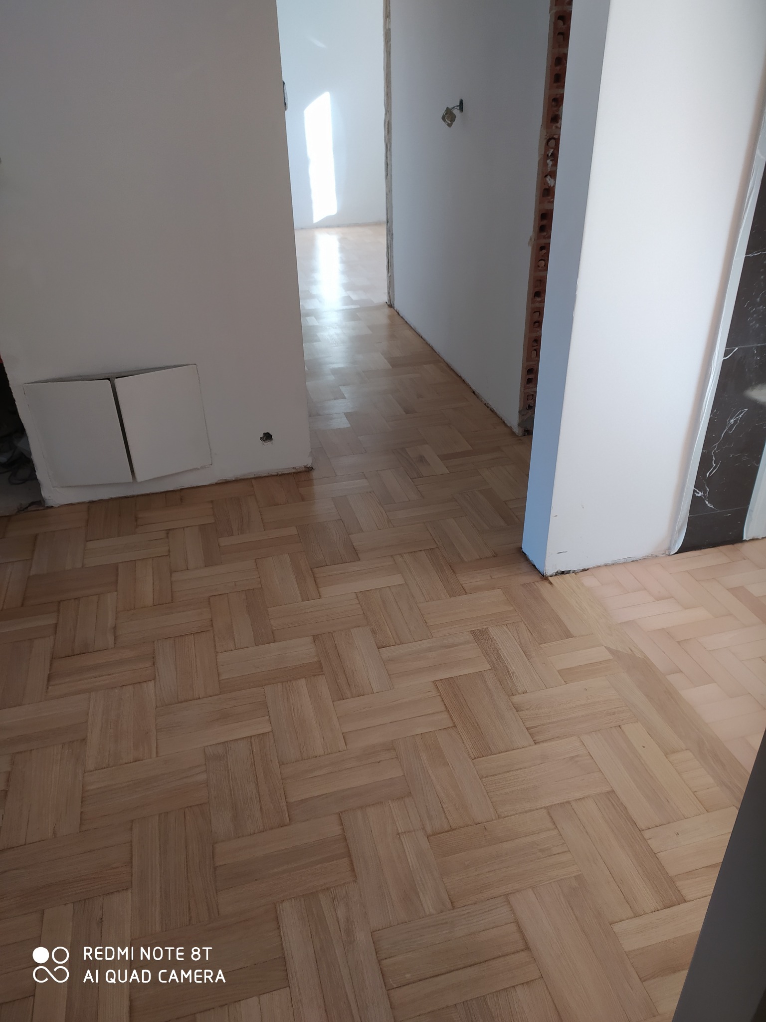 Ułożony parkiet w jodełkę francuską w jasnym odcieniu, widoczne niedokończone ściany i przygotowania do wykończenia wnętrza.