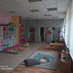 AKADEMIA MALUCHA DANUTA SKOMOROWSKA-LEŹNICKA - Wnętrze sali zabaw z kolorowymi motylami zawieszonymi pod sufitem, regałami z zabawkami, dywanami z postaciami z bajek i stolikami dla dzieci.
