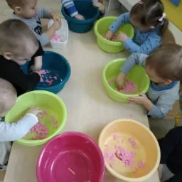 Dzieci w Olsztynie bawią się kolorowym piaskiem kinetycznym w miskach na stole podczas zajęć sensorycznych.