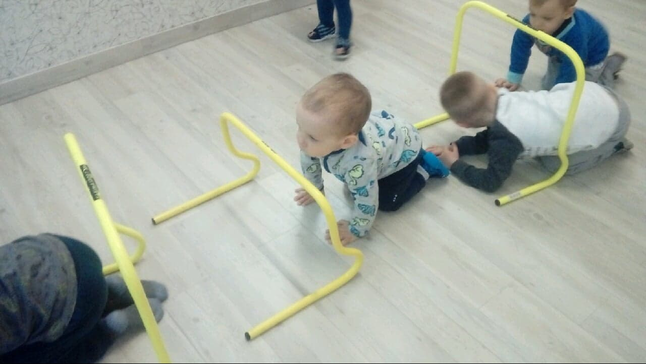Dzieci raczkują pod żółtymi przeszkodami na podłodze w żłobku, ćwiczenia motoryczne.