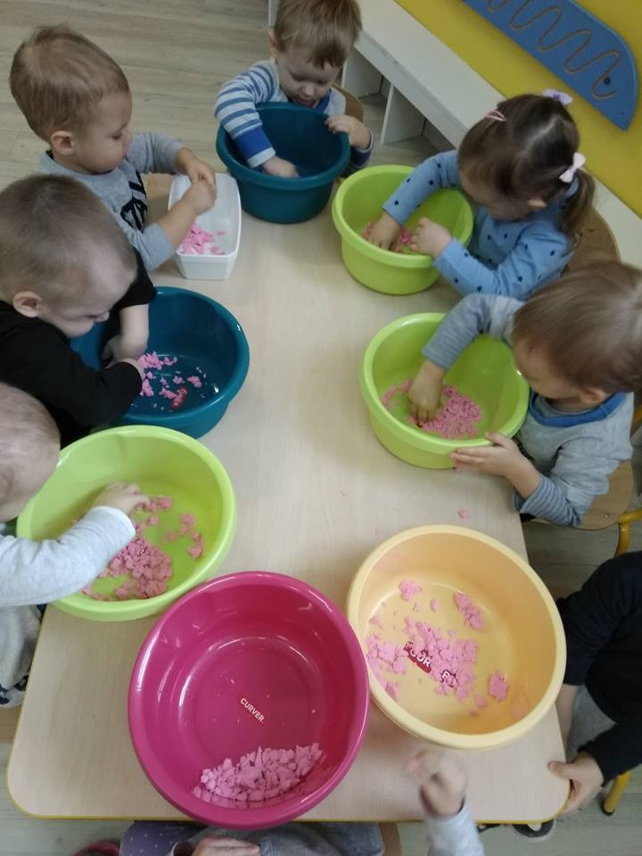 Dzieci w Olsztynie bawią się kolorowym piaskiem kinetycznym w miskach na stole podczas zajęć sensorycznych.
